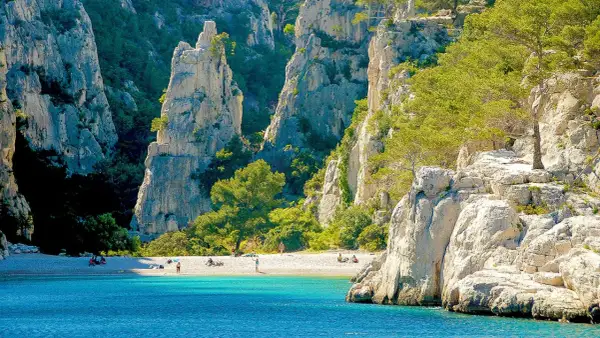 Sonnige Bucht mit türkisfarbenem Wasser und Felsen, ideal zum Calanques Baden. Menschen entspannen am Strand.